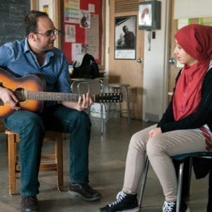 Teaching artist Ami Yares playing guitar with a singing student in a classroom