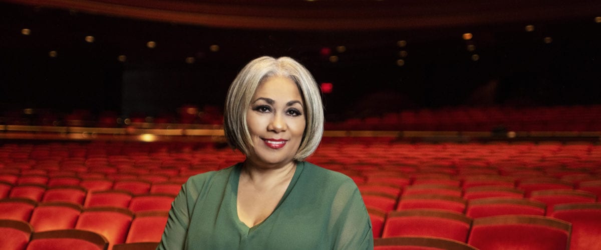 Dyana Williams sits at the edge of a row of seats in the audience of a theater.