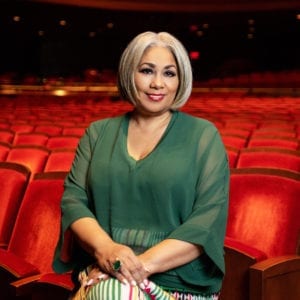 Dyana Williams sits at the edge of a row of seats in the audience of a theater.